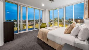 A bedroom with a large bed, a desk, and a chair. It has large windows with a city view. - Exclusive Stays - Southgate (Southbank)