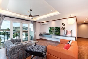 Ein modernes Wohnzimmer mit Sofa, Sessel und Fernseher an der Wand.