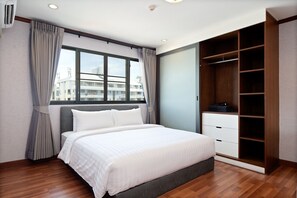 Ein Schlafzimmer mit Bett, Fenster, Kleiderschrank und Blick auf Gebäude.