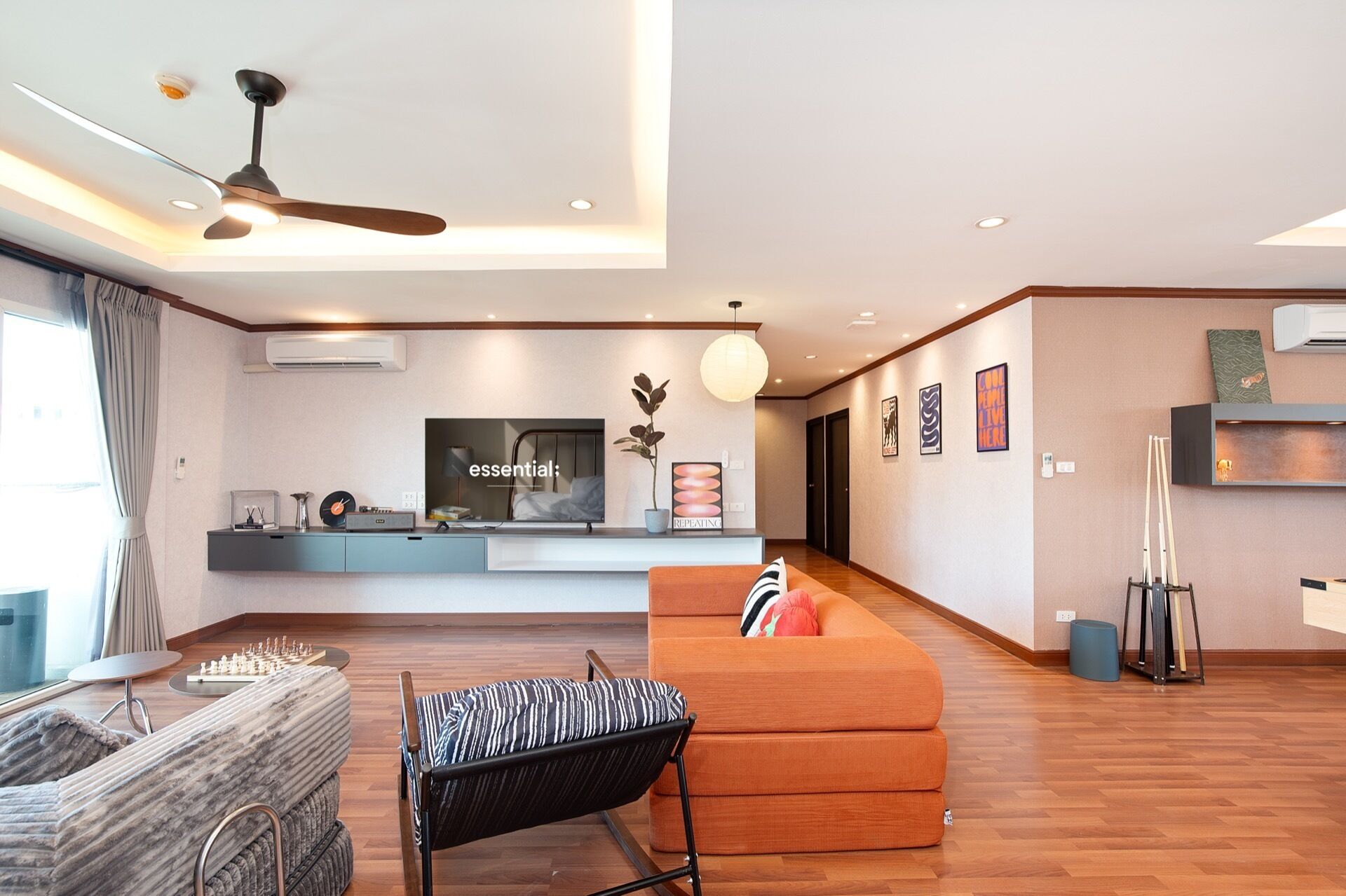 Una sala moderna con un sofá, una silla, un ventilador de techo y un televisor de pantalla plana.