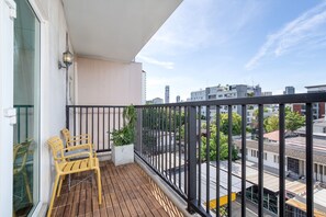 Ein Balkon mit Holzboden, zwei gelbe Stühle, einem Blumentopf und Blick auf die Stadt.