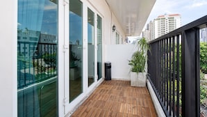 A balcony with a wooden floor, glass doors, a potted plant, and a trash bin. - Capitel Ekkamai Hotel (Bangkok)