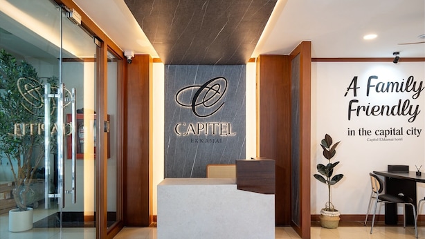 A hotel reception area with a reception desk, a bed, a wall with a logo, and a sign stating 'A Family Friendly in the capital city'. - Capitel Ekkamai Hotel (Bangkok)
