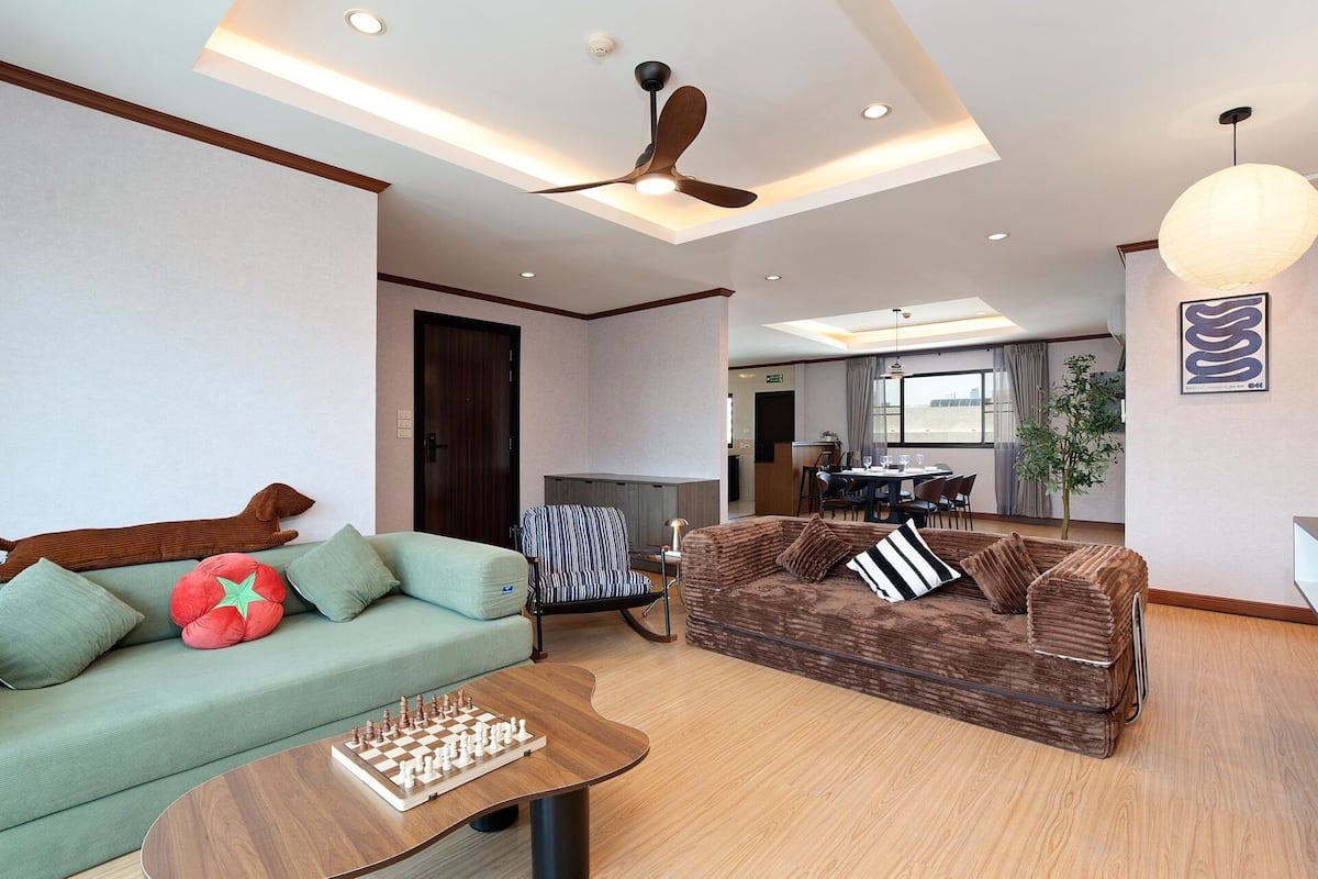 Ein Wohnzimmer mit einer Couch, einem Couchtisch mit einem Schachspiel, einem gestreiften Sessel und einem Deckenventilator.