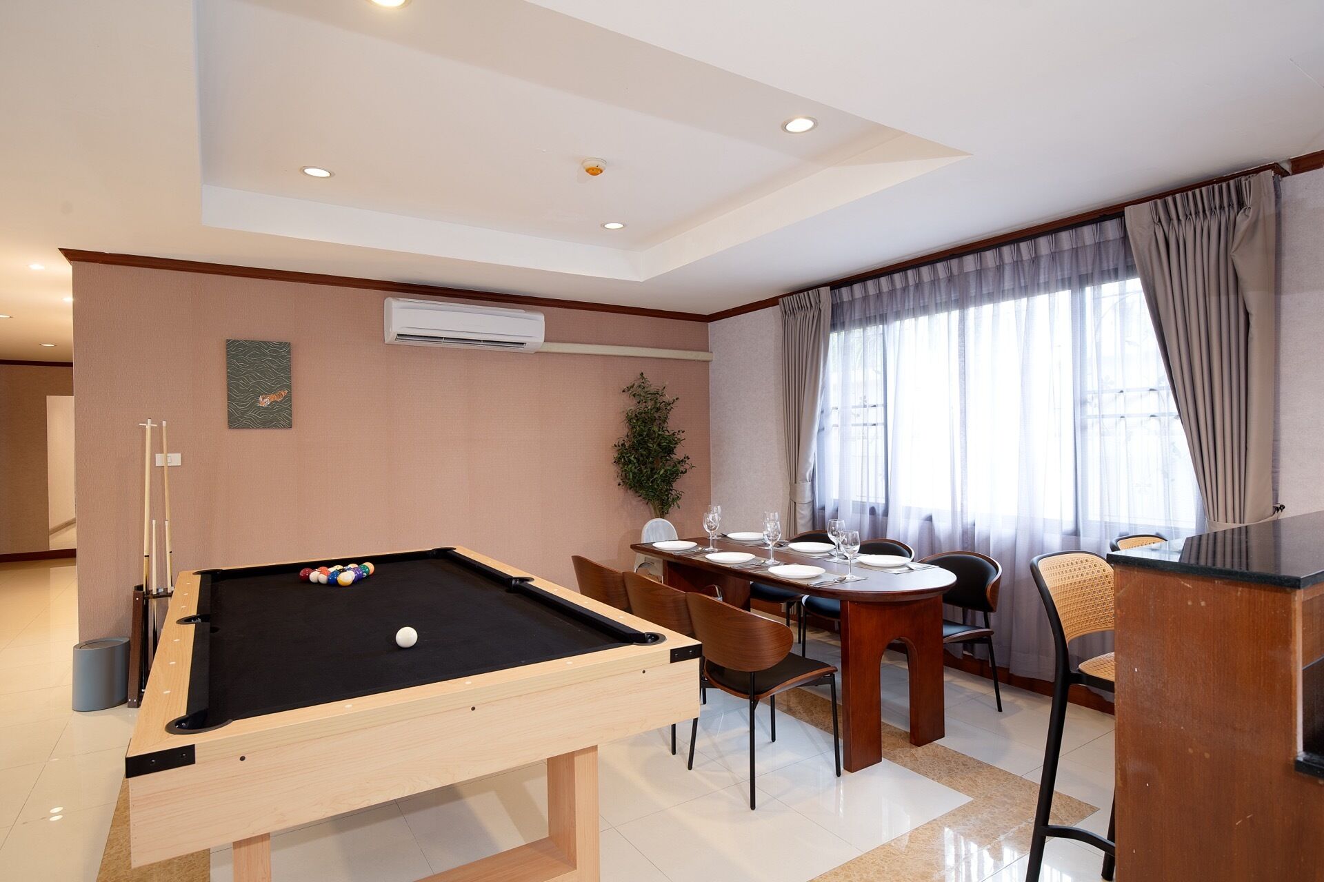 A room with a pool table, dining table, chairs, and a bar area.