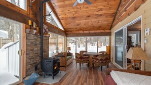 Un intérieur de chalet chaleureux avec une cheminée en pierre, un plancher en bois, un coin repas et de grandes fenêtres.