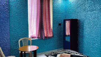 Una habitación con cama, una silla, una mesita, una ventana con cortinas y un armario.