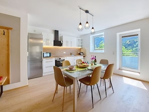 A modern kitchen with stainless steel appliances, a dining area with a glass table and chairs, and a large window with a view of greenery. - Halbeis by Interhome (Matrei am Brenner)