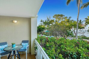 A balcony with a table and chairs, a potted plant, and a view of a landscaped area with trees and shrubs. - Oceanfront Gem at Trinity Beach - Pool - Sea View (Trinity Beach)