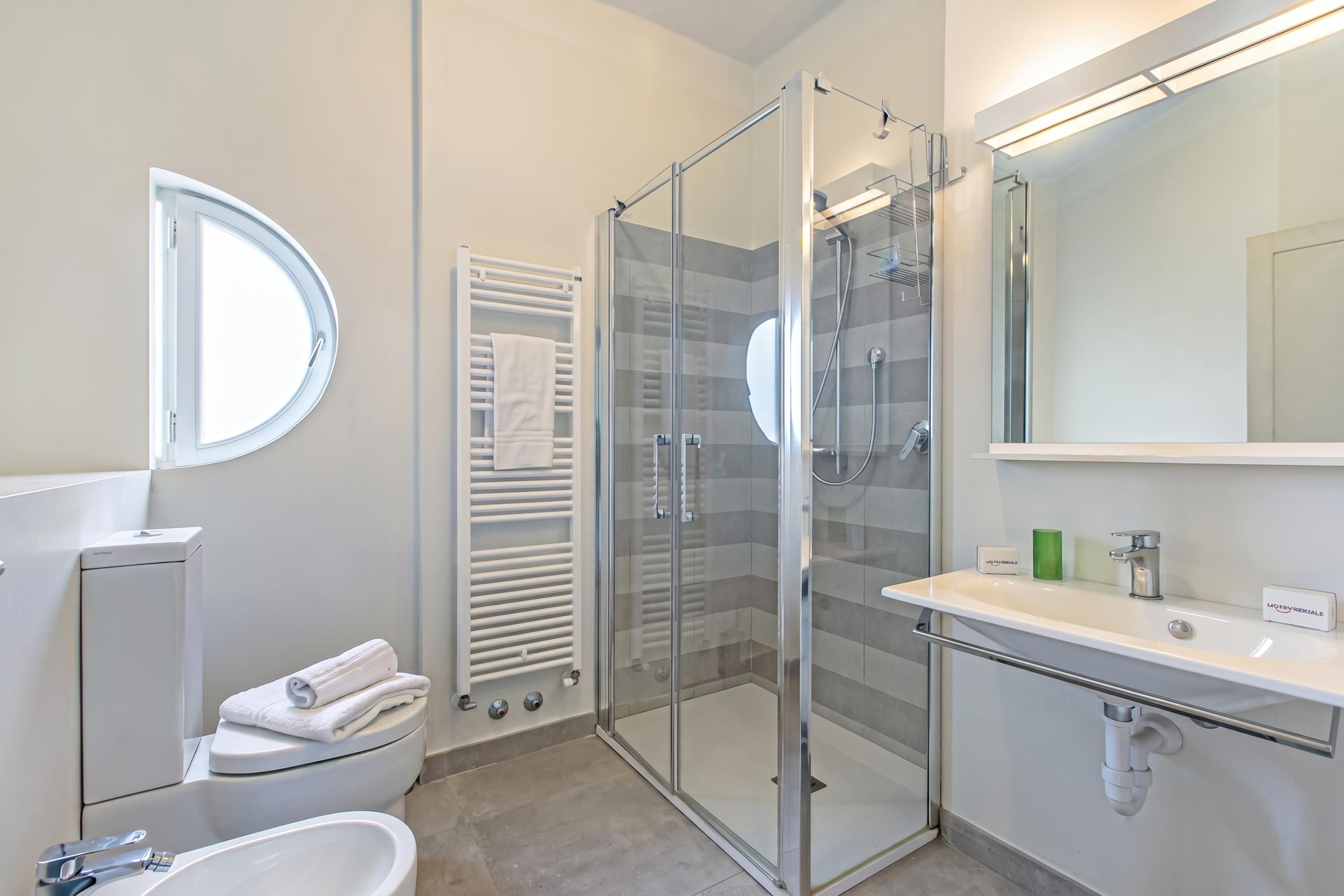 Un bany modern amb un espai de banyera de vidre, un lavabo blanc amb un mirall i un vàter amb una tovallola.