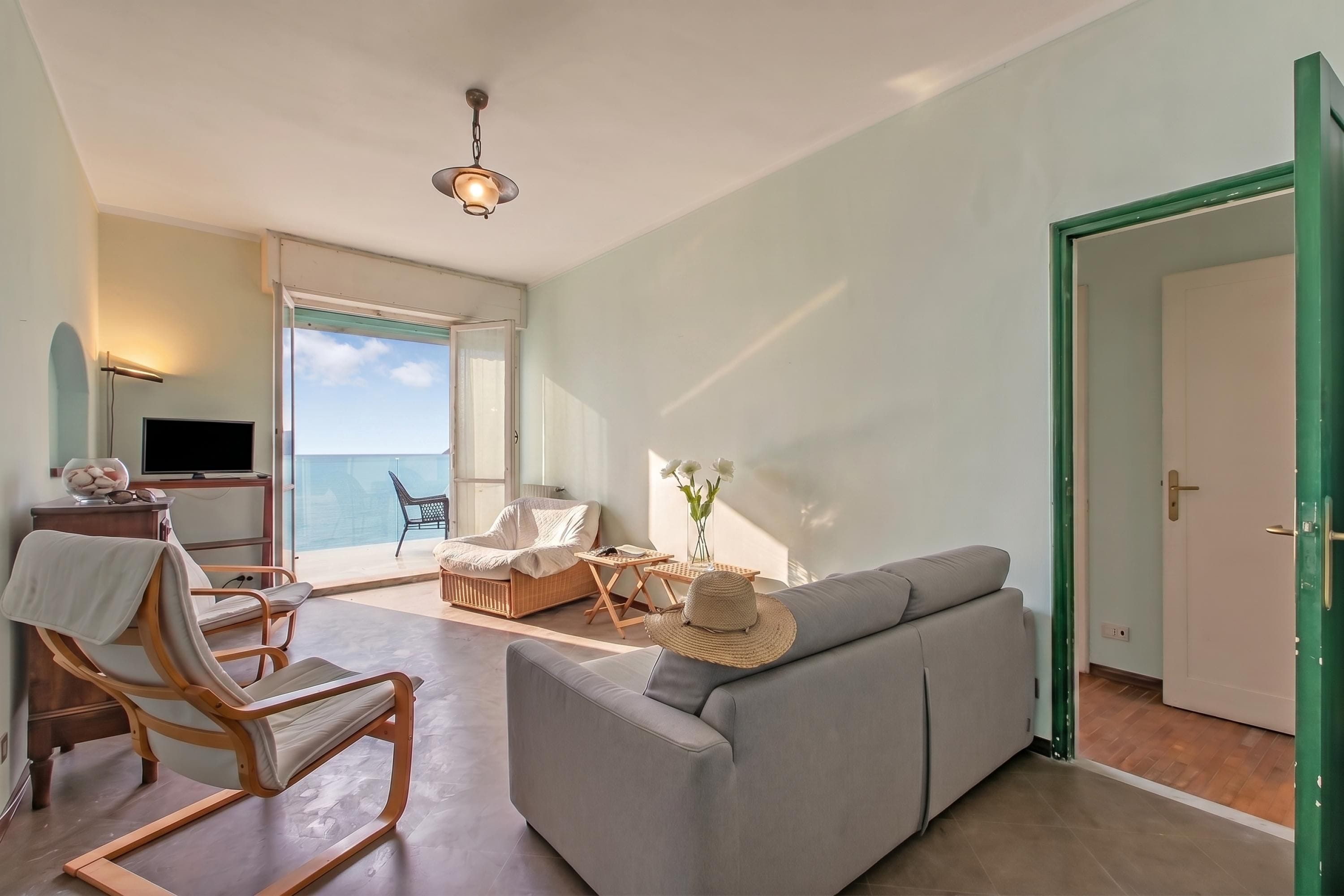 A living room with a sofa, a chair, a small table, a TV, and a view to the outside.