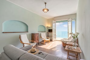 A room with a sofa, two rocking chairs, a small table with a vase and flowers, and a view of the sea through an open door. - Attico Giancardi (Alassio)