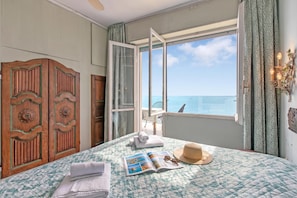 A bedroom with a bed, a window with a view of the sea, a wardrobe, and a door leading to a balcony. - Attico Giancardi (Alassio)