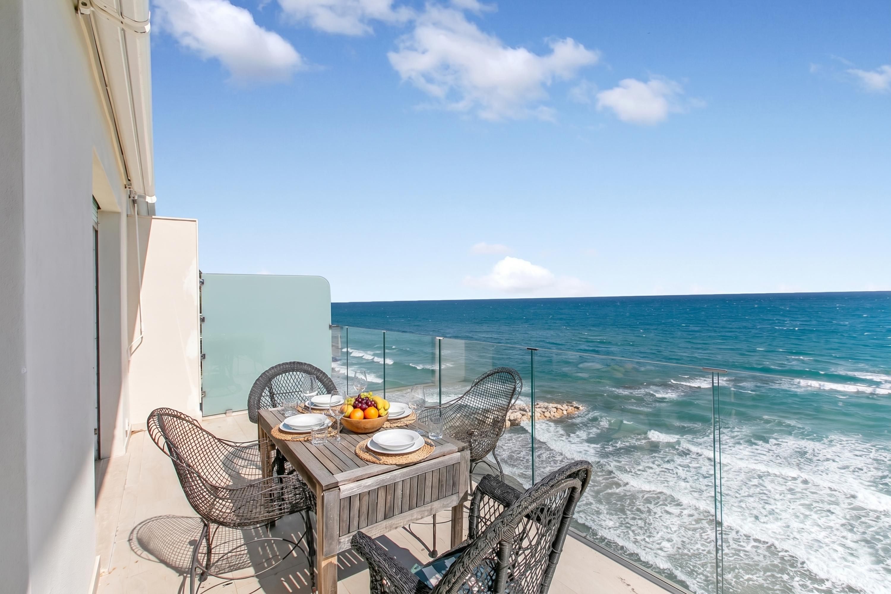 A balcony with a table set for dining, overlooking the ocean.