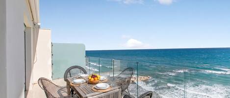 A balcony with a table set for dining, overlooking the ocean.