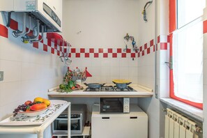 A compact kitchen with a gas stove, microwave, oven, and a bowl of fruit on the counter. - Attico Giancardi - Beachfront Sea-view Terrace (Alassio)
