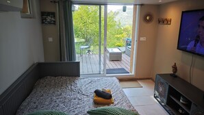 Ett sovrum med en säng, en tv, en balkong med utemöbler och utsikt över grönområden.
