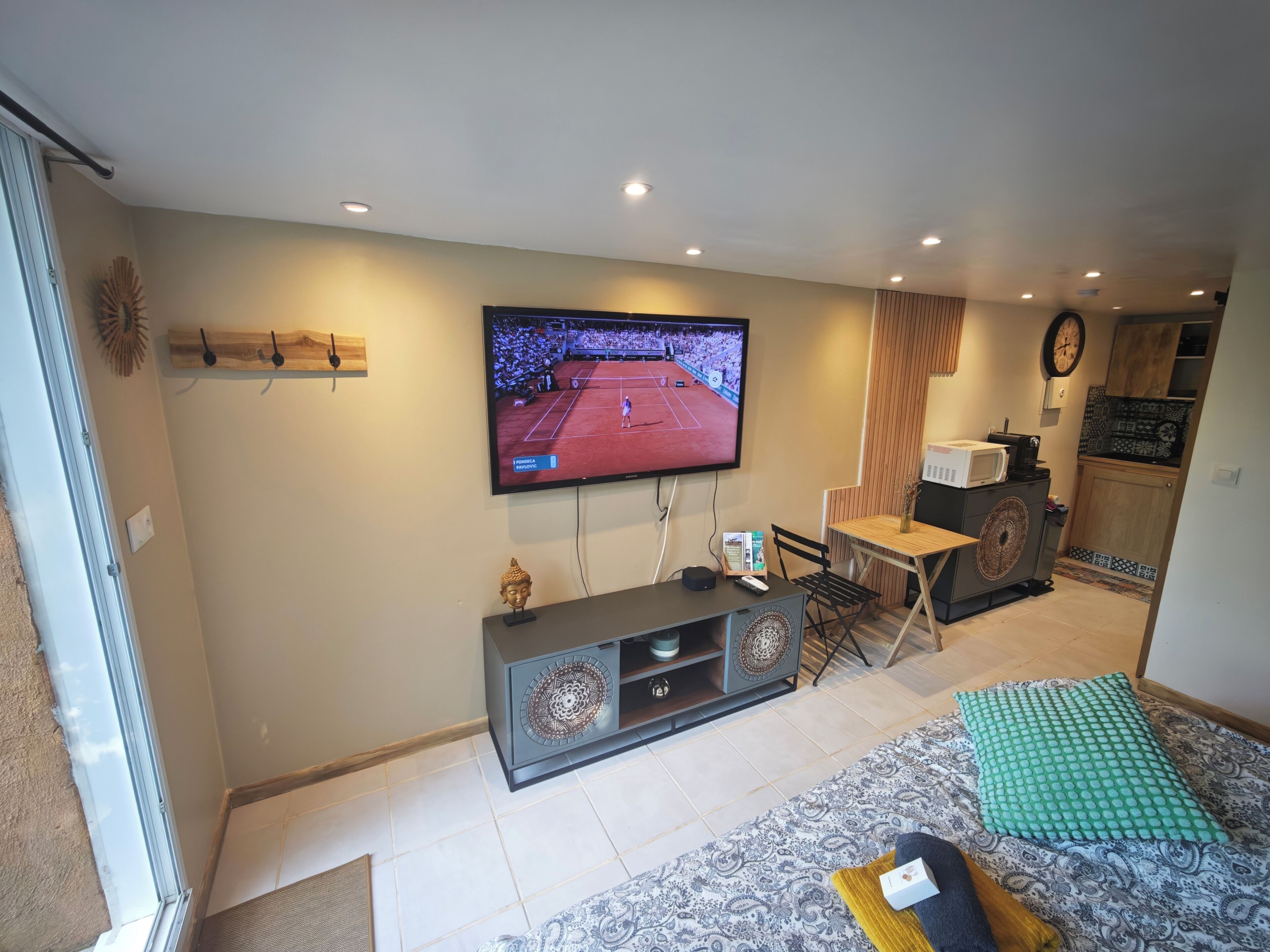 Una sala de estar con televisor, sofá, una mesita y una zona de cocina al fondo.