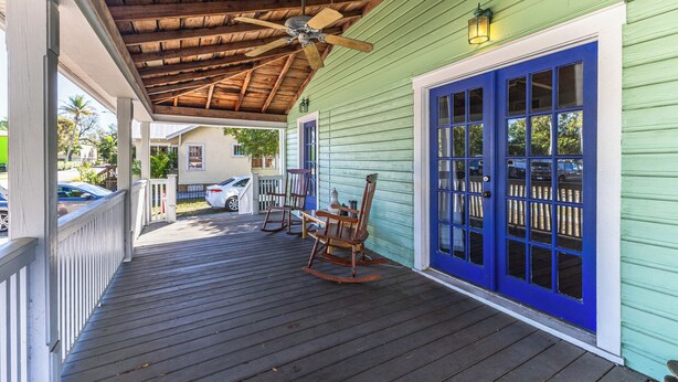 Un portico in legno con una ventola a soffitto, poltrone a dondolo e una porta blu.