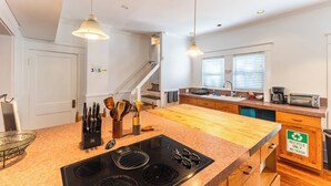 Una cucina moderna con isola centrale, piani di lavoro in legno, piano cottura integrato e un cartello che indica solo raccolta differenziata.