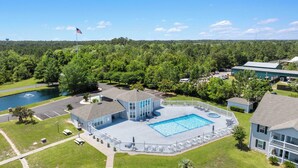 A building with a swimming pool, surrounded by a fence, and a flagpole with an American flag. - Gulf Shores Condo with Pool & Hot Tub (Gulf Shores)