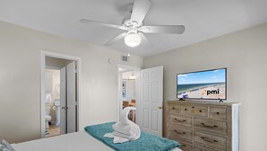 A bedroom with a bed, a ceiling fan, a television on a dresser, and a door leading to a bathroom. - Gulf Shores Condo with Pool & Hot Tub (Gulf Shores)