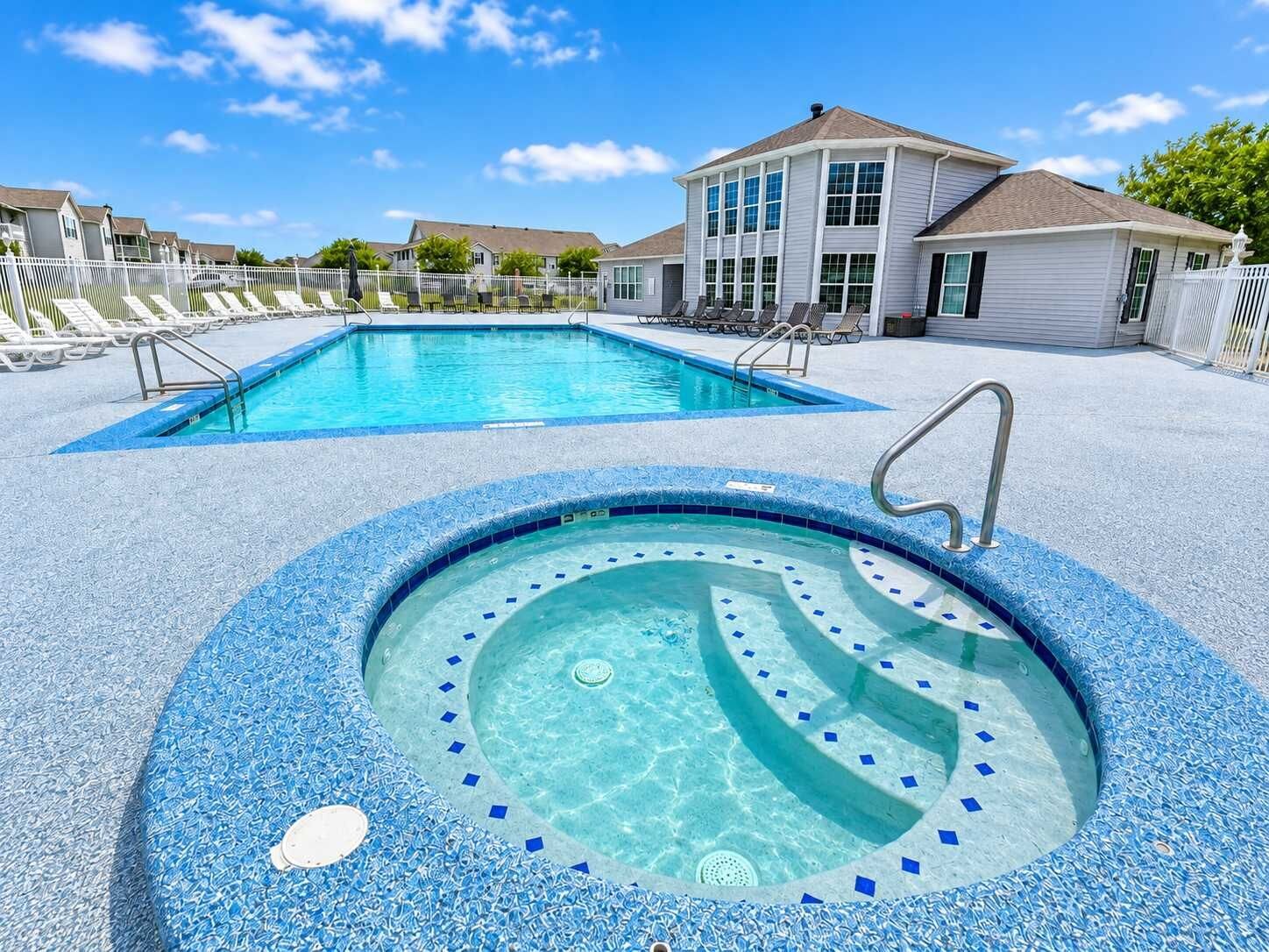 A swimming pool with a hot tub, surrounded by lounge chairs and a building with large windows.