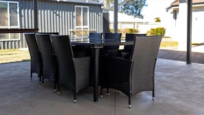 Een overdekt terras met een ronde tafel en zes stoelen.