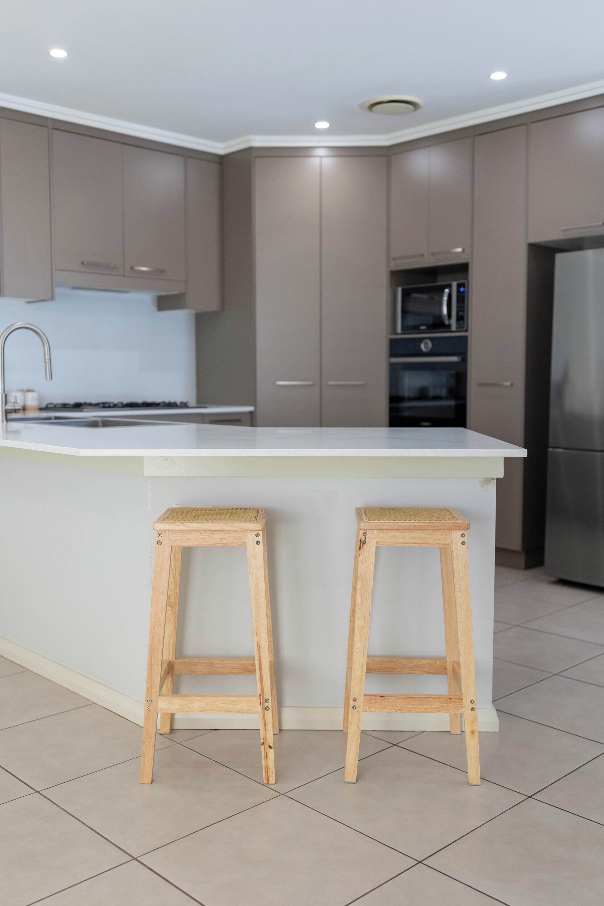 Uma cozinha moderna com ilha central, dois banquetes de madeira, eletrodomésticos de aço inoxidável e armários em tons claros.