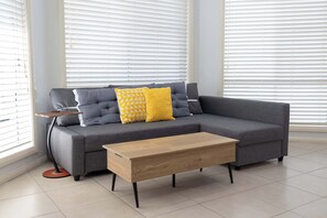 A modern living room with a grey sofa, yellow patterned pillows, a wooden coffee table, and a side table with a lamp.