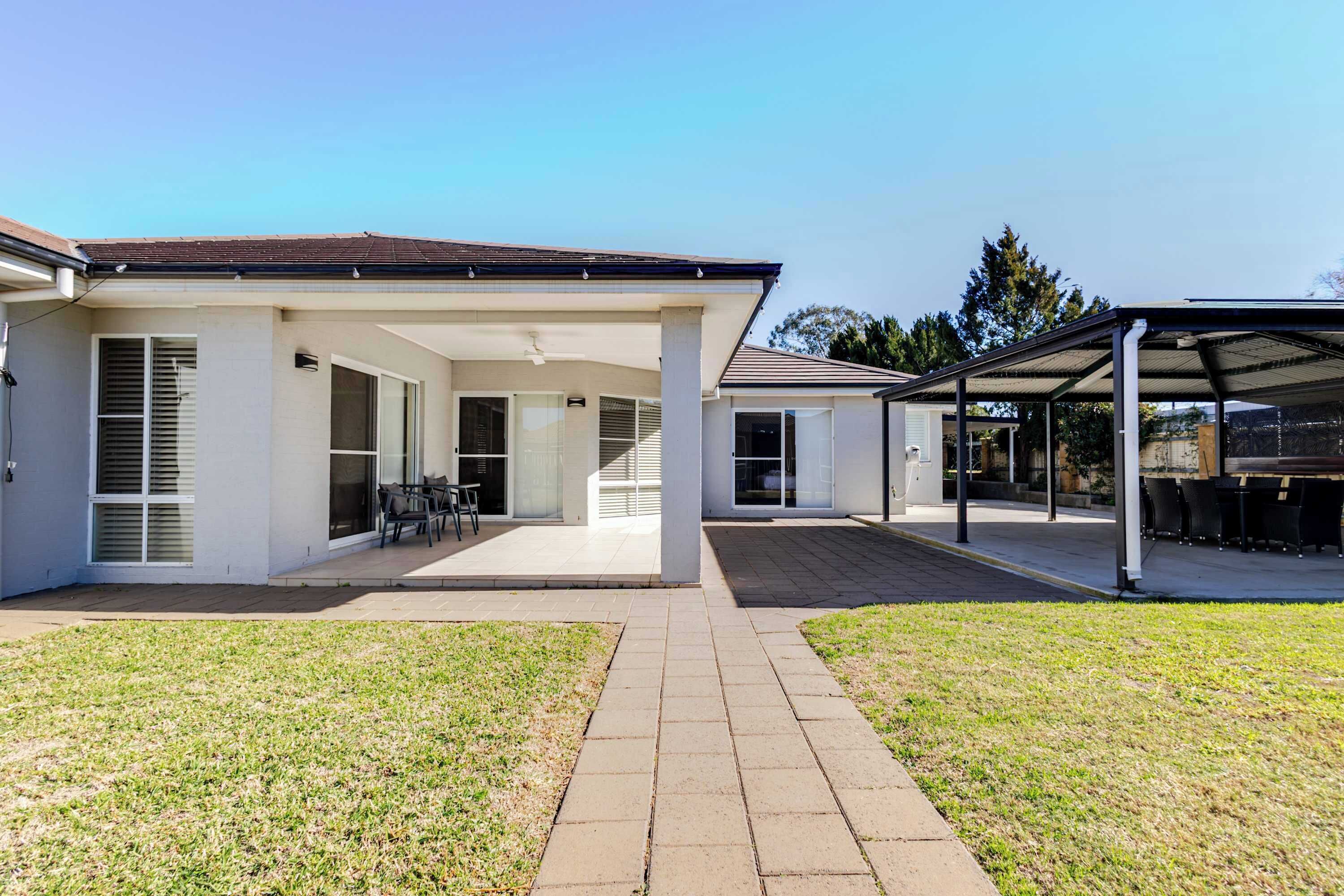 A modern two-story house with a covered patio area, a paved driveway, and a well-maintained lawn.