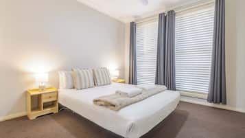 A hotel room with a bed, two bedside tables, a lamp, and a large window with curtains.