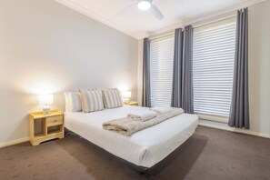 A hotel room with a bed, two bedside tables, a lamp, and a large window with curtains.