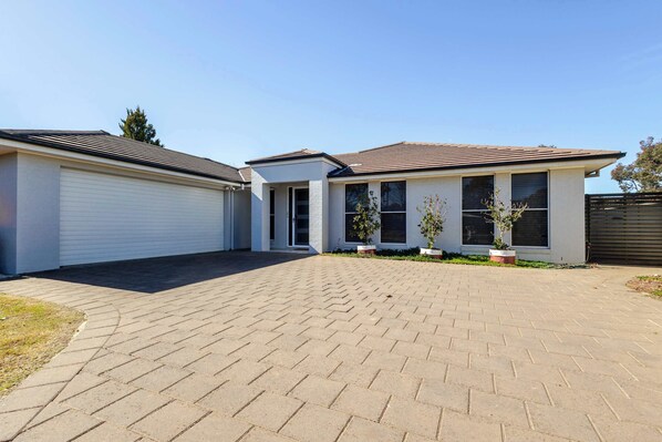 A two-story residential building with a paved driveway and potted plants.