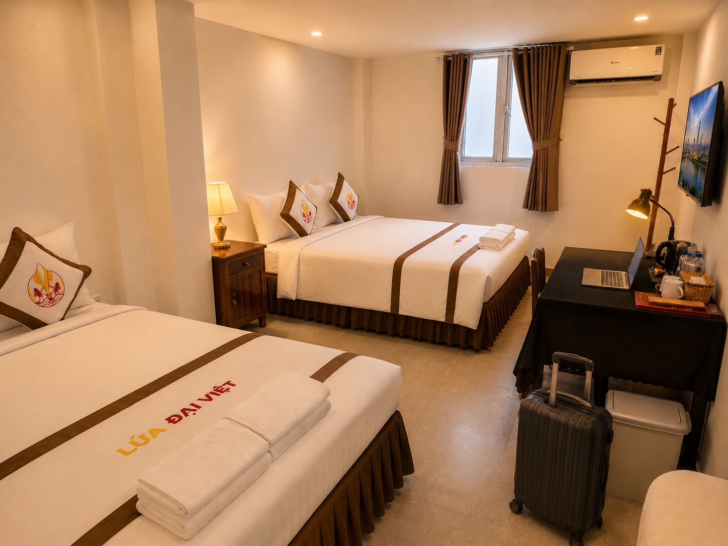Habitación de hotel con dos camas, un escritorio, una computadora portátil, una maleta y un aire acondicionado.