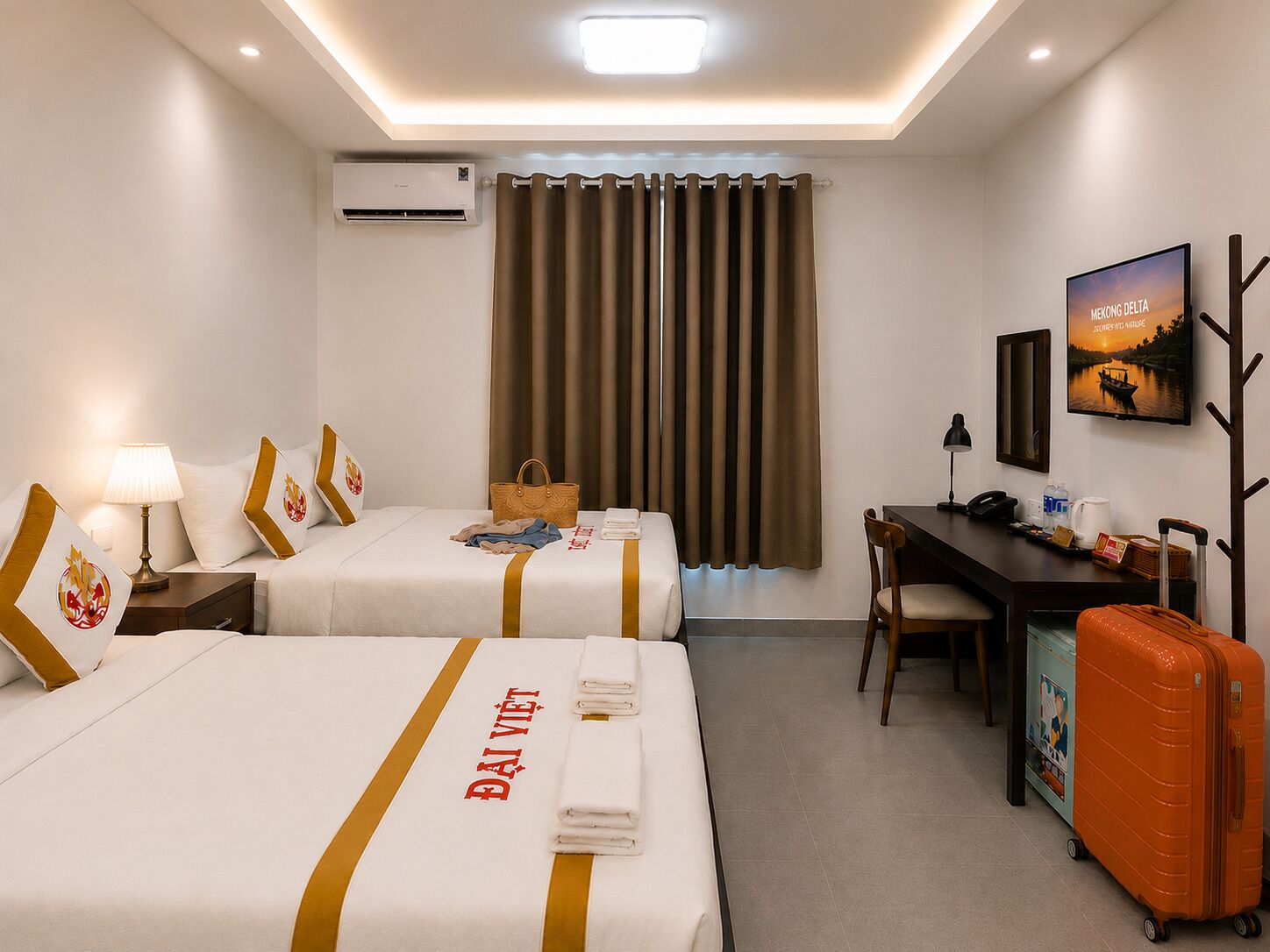 A hotel room with two beds, a desk, a chair, an air conditioner, a window with curtains, a television, and a suitcase.
