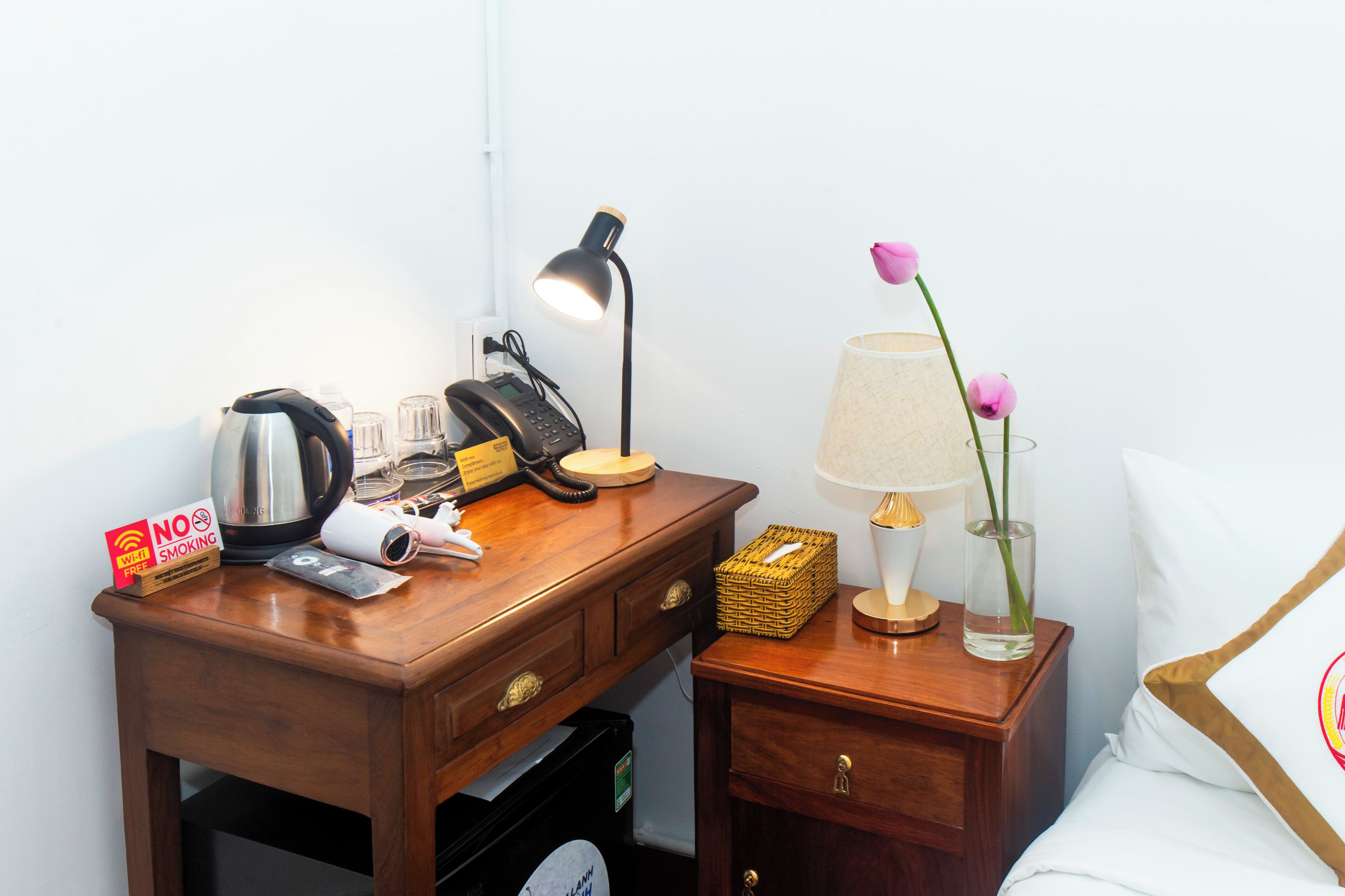 A wooden desk with a kettle, a lamp, a phone, and a 'No Smoking' sign.
