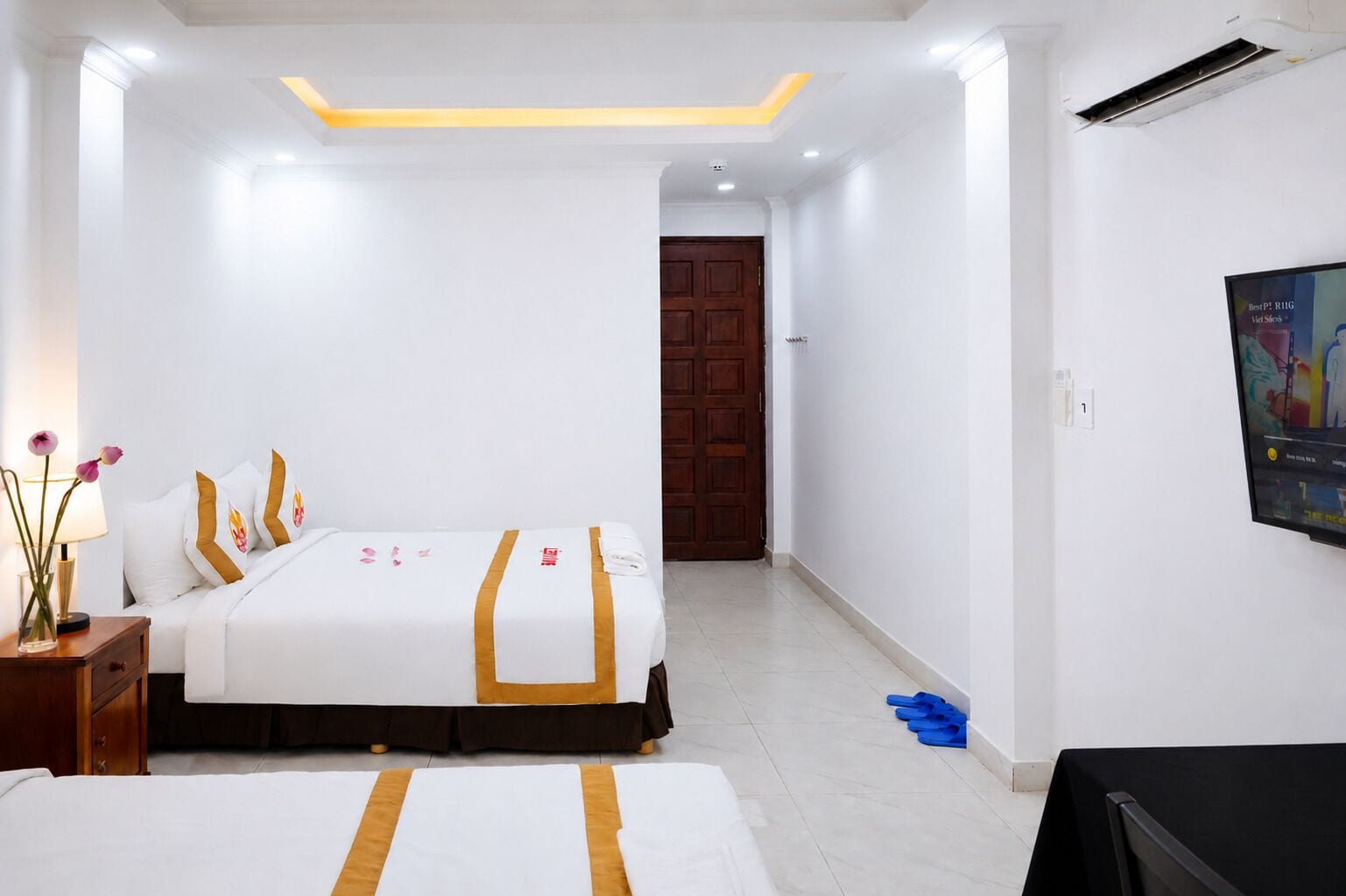 Una habitación de hotel con cama, televisor, mesita de noche de madera y una puerta que da a otra habitación.