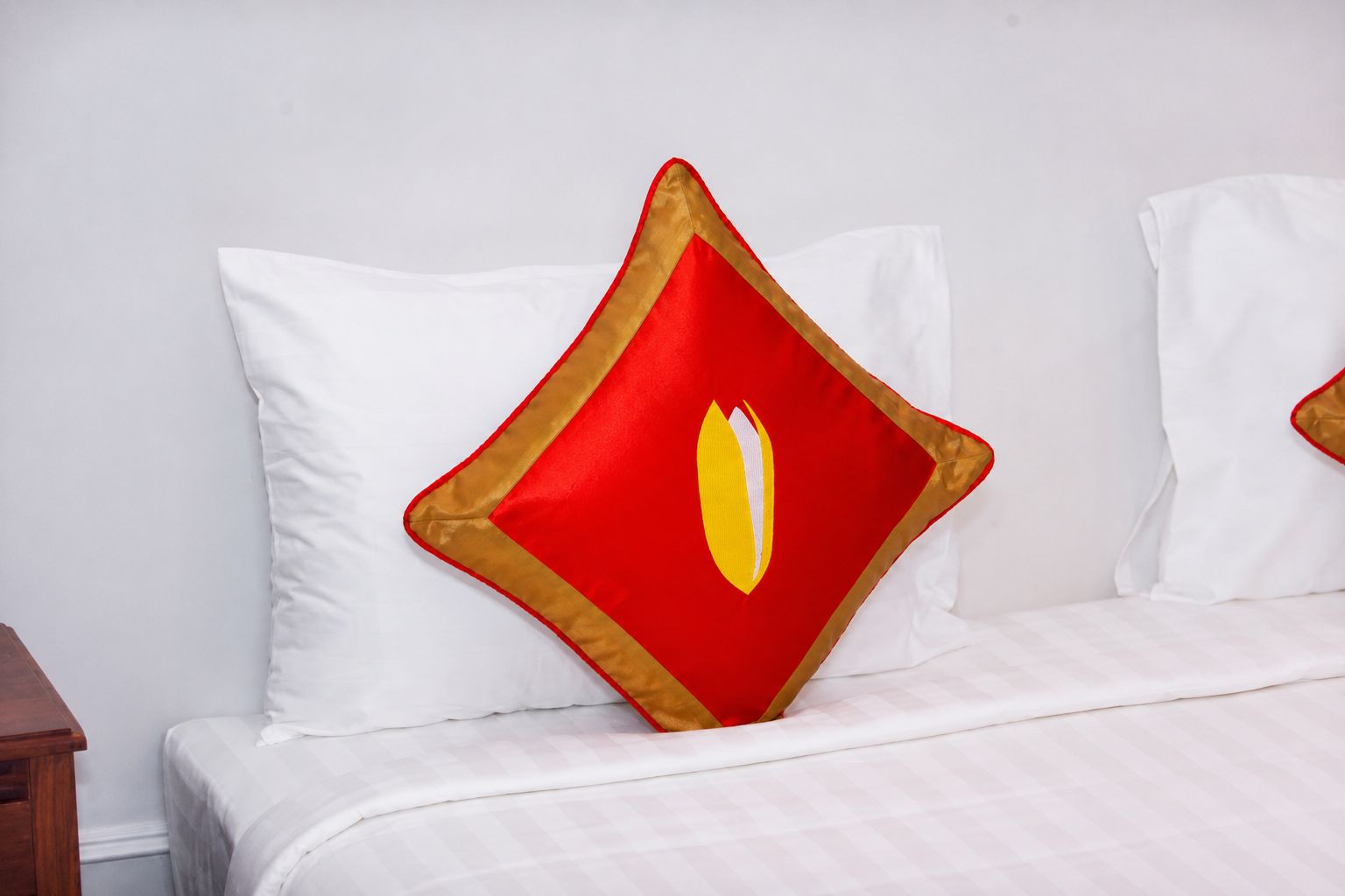 A bed with white bedding and a single red and gold pillow with a yellow emblem.