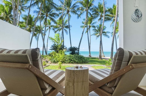 Ein Zimmer mit zwei gestreiften Lounge-Stühlen mit Blick auf einen Strand, an dem Palmen stehen, und einen klaren Meerblick.