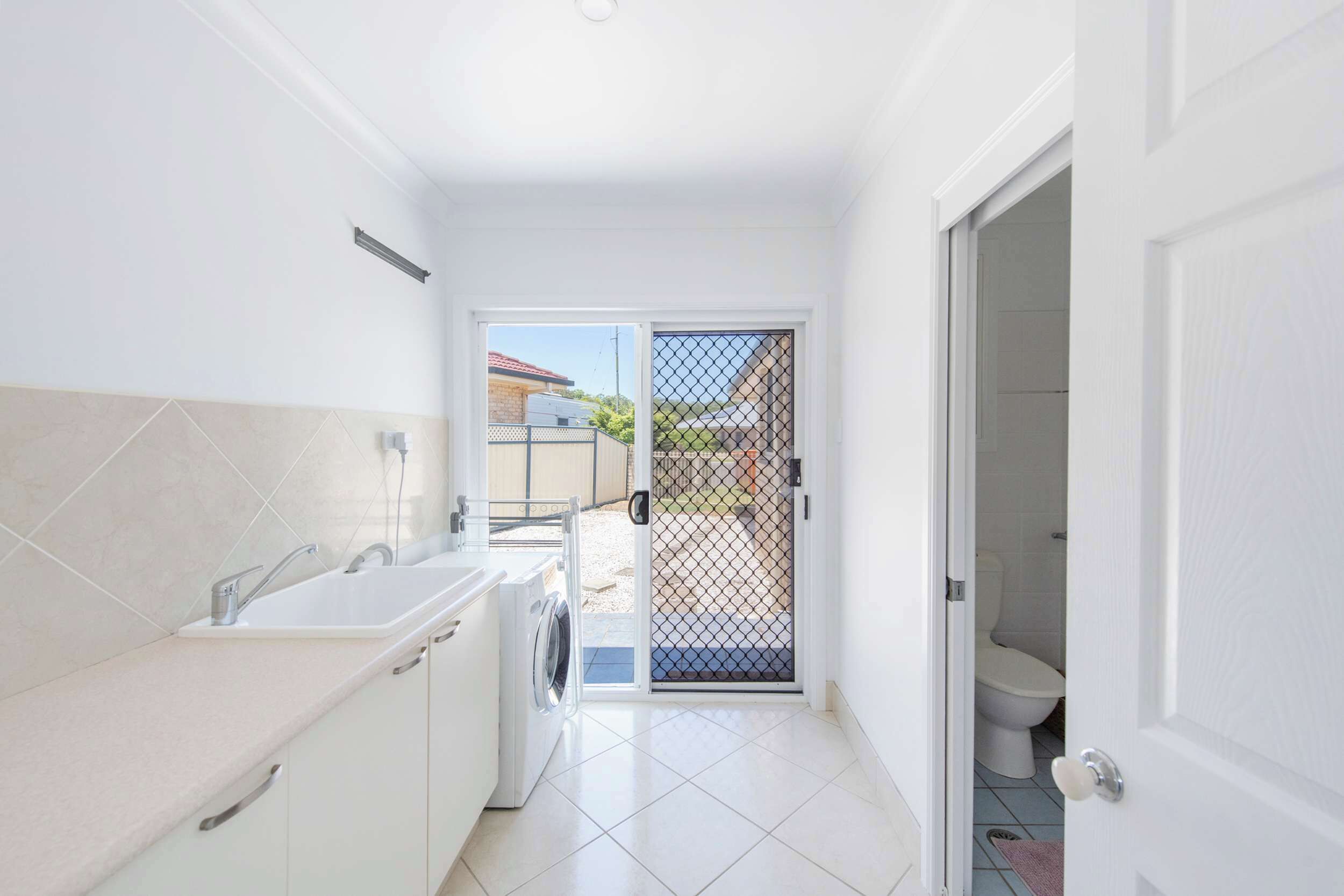 A compact kitchen with a washing machine, a sink, and a door leading to a balcony.