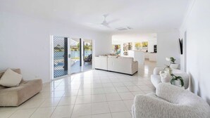 A spacious living area with a sofa, a white armchair, and a kitchen in the background. - Little Casa - Oceanstays - Pool & Boat Ramp (Yamba)