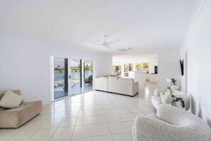 A spacious living area with a sofa, a white armchair, and a dining area in the background. - Little Casa - Oceanstays - Pool & Boat Ramp (Yamba)