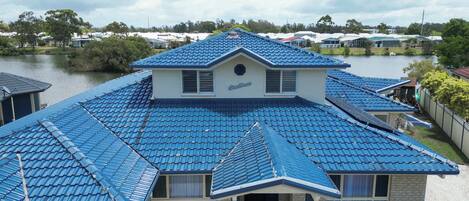 A house with a blue tiled roof, a central chimney, and a view of a lake.
