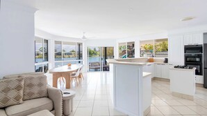 A modern kitchen with a central island, white cabinetry, and a dining area with a round table and chairs. - Little Casa - Oceanstays - Pool & Boat Ramp (Yamba)