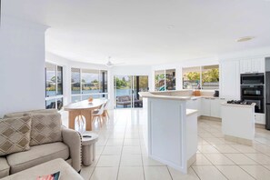 A modern kitchen with a central island, white cabinetry, and a dining area with a round table and chairs. - Little Casa - Oceanstays - Pool & Boat Ramp (Yamba)