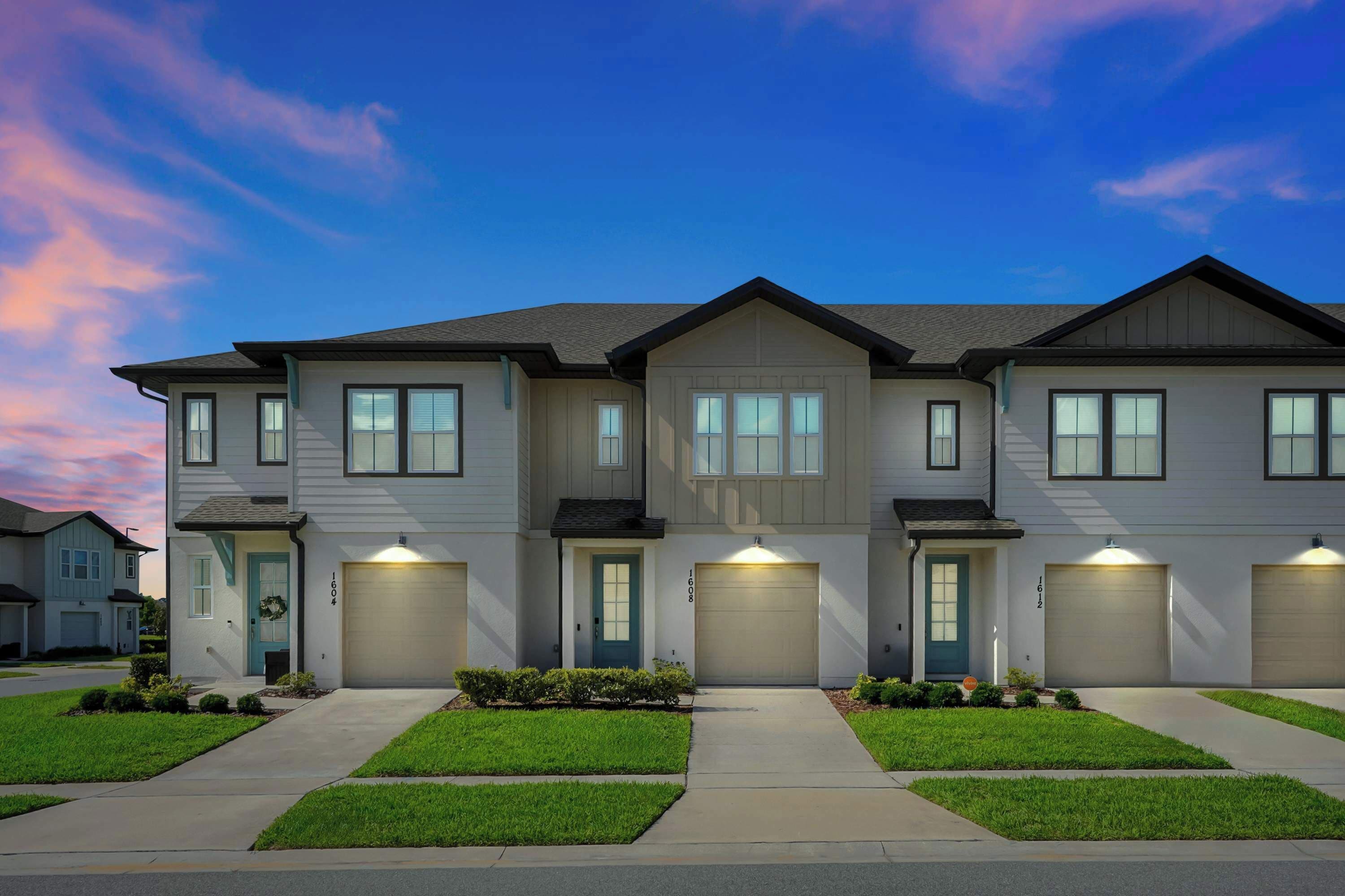 A row of modern two-story townhouses with front garages, a well-maintained lawn, and a clear sky.