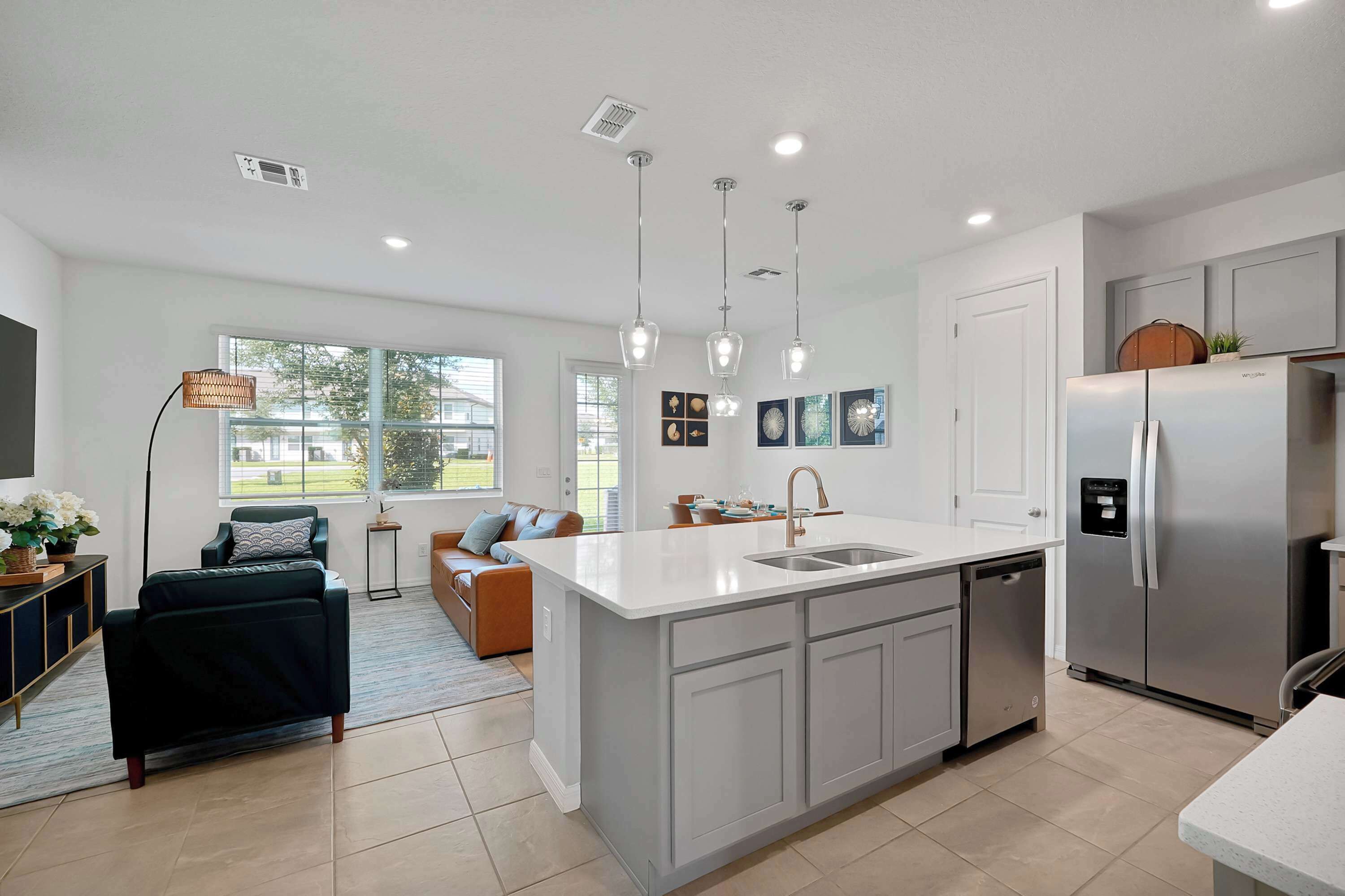 A modern kitchen with a central island, stainless steel appliances, pendant lighting, and a view to the outdoors.