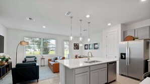 A modern kitchen with a central island, stainless steel appliances, pendant lighting, and a view to the outdoors. - Modern Villa Near Disney, Resort Splash Park (CHAMPIONS GT)
