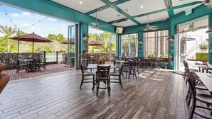 An outdoor patio area with wooden flooring, tables, chairs, and umbrellas. - Modern Villa Near Disney, Resort Splash Park (CHAMPIONS GT)